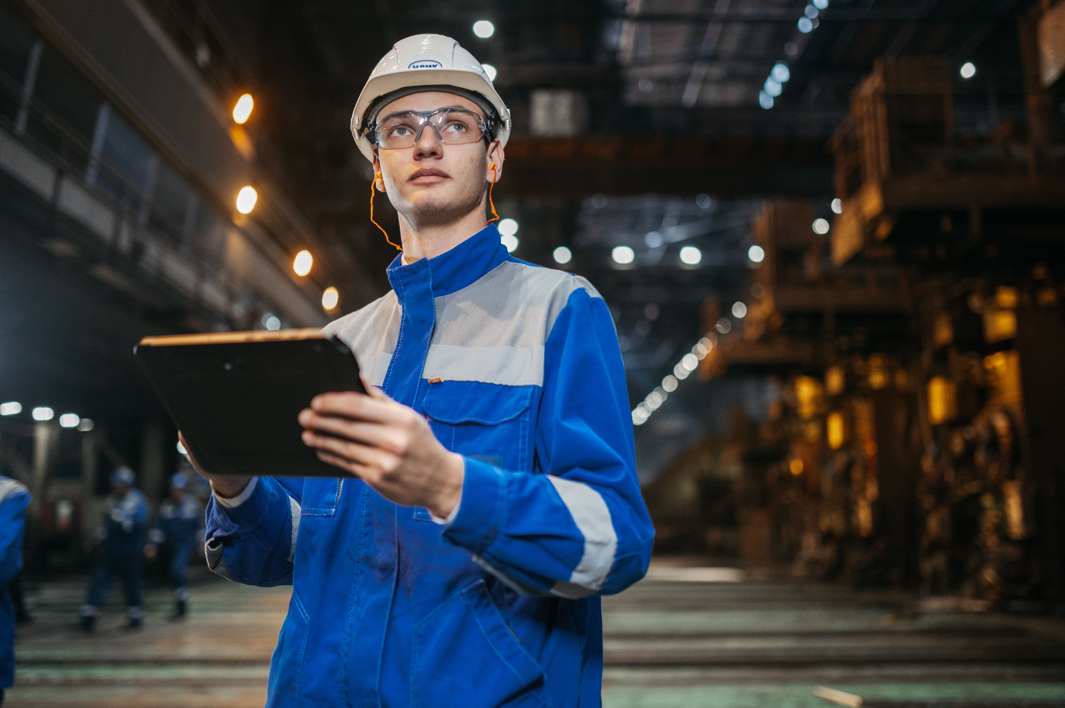 Engineer in safety gear inspecting factory equipment with a tablet